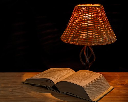 A person reading a book at night with a warm bedside lamp